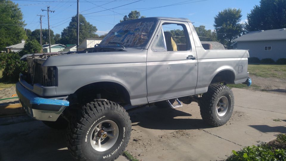 Gray Ford Bronco with lifted suspension and off-road tires, hood open, front bumper taped