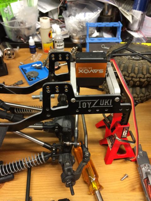 1989 Ford Bronco - Close-up of an RC car's chassis assembly, a Savox servo and Toyzuki components, surrounded by tools on a workbench.