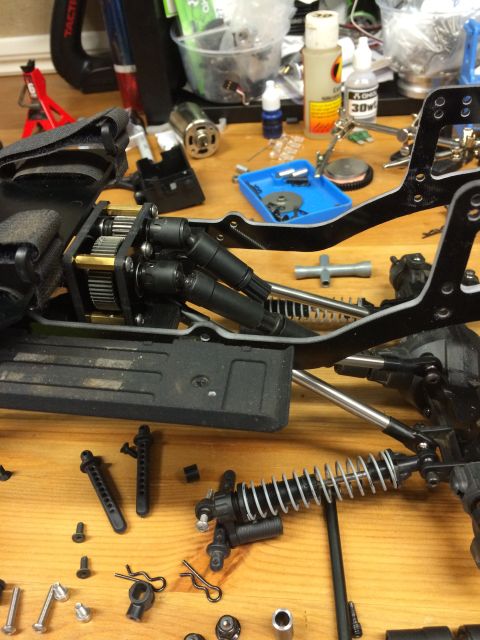 1989 Ford Bronco - Close-up view of an RC car's chassis, its internal drivetrain and suspension system components laid out on a workbench.