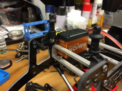 1989 Ford Bronco - A component of a radio-controlled car, a Savox servo and carbon fiber parts, sits on a workbench.