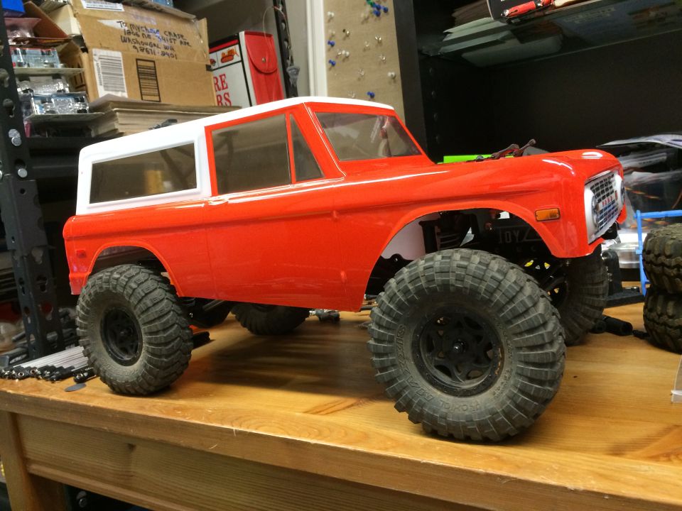 Red and white RC model Bronco with large off-road tires on a wooden table