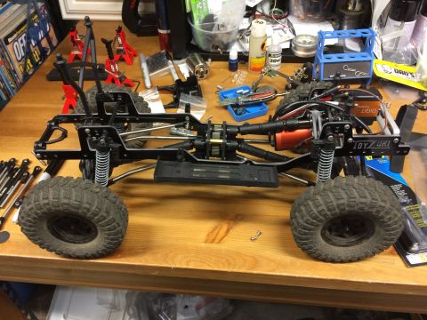 1989 Ford Bronco - A remote control car chassis is assembled on a workbench with various tools and parts scattered around.