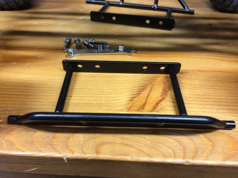 1989 Ford Bronco - RC car parts, including a roll cage section and mounting hardware, laid out on a wooden table.