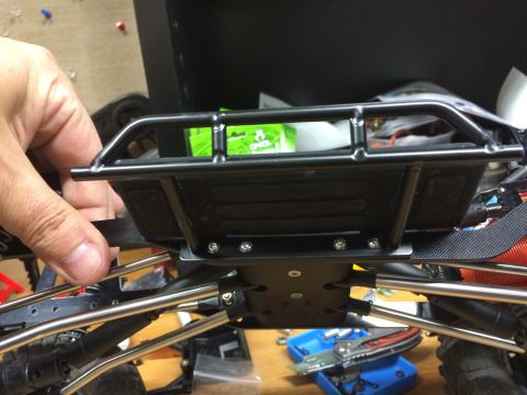 1989 Ford Bronco - Close-up view of the chassis and bumper assembly of a remote-controlled vehicle, with a hand adjusting a strap.