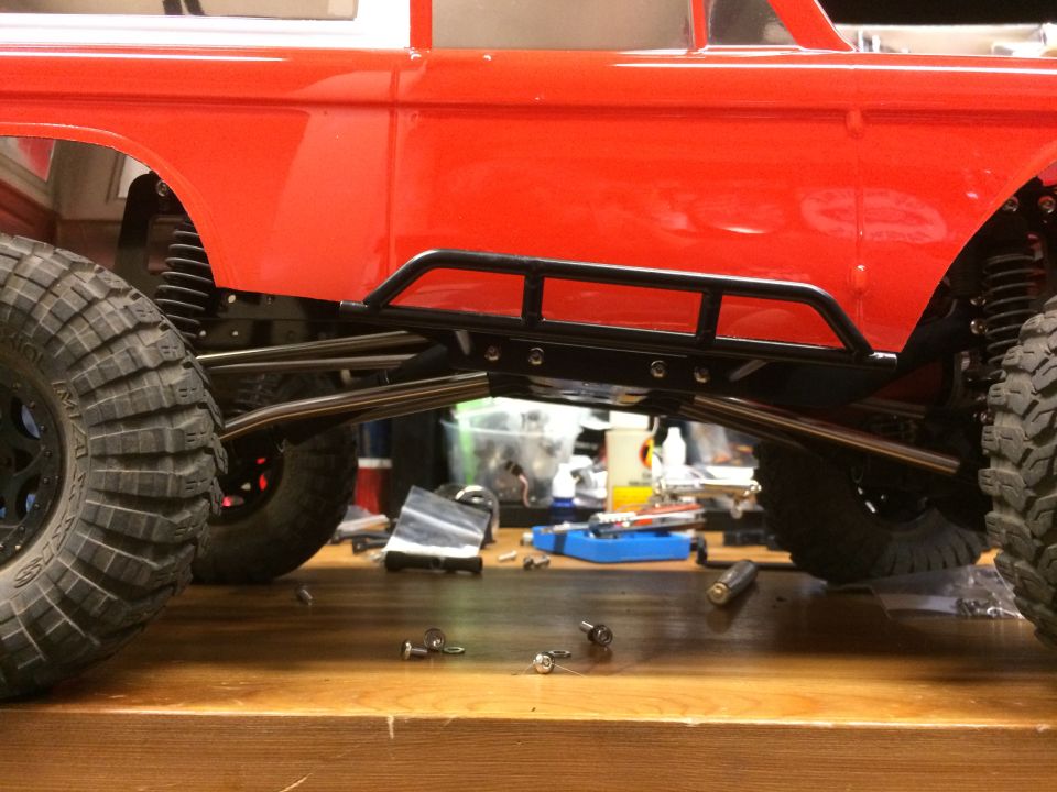 RC car chassis with large off-road tires and side rock sliders, parts scattered on workbench