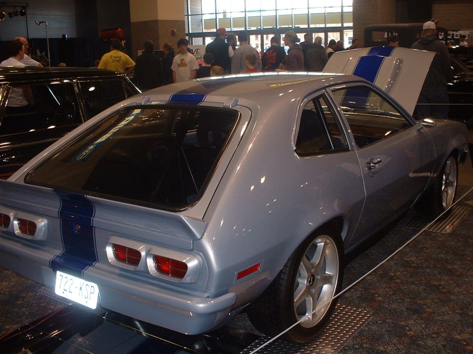 Silver hatchback coupe with blue racing stripes and round taillights on a show stand indoors