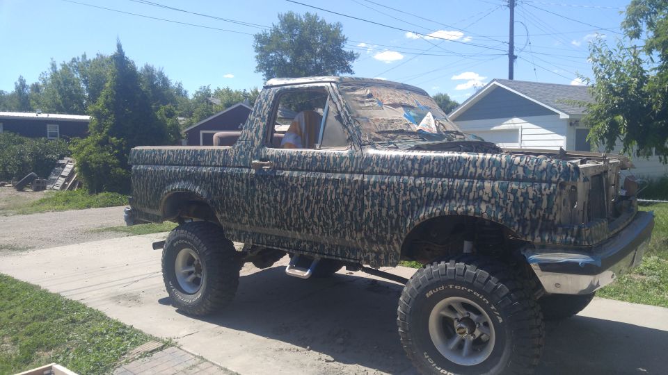 Camouflaged Ford Bronco with lifted suspension and off-road tires parked on a driveway