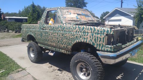 1991 Ford Bronco - This lifted pickup truck features a camouflage paint job and its front end is missing the grille and headlights.