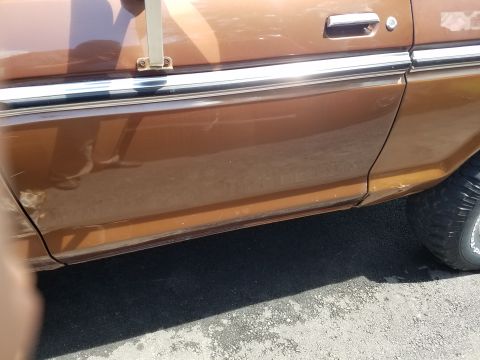 1979 Ford Bronco - Side view of a brown 1978 Ford Bronco, showing the door panel and tire with visible wear and tear.
