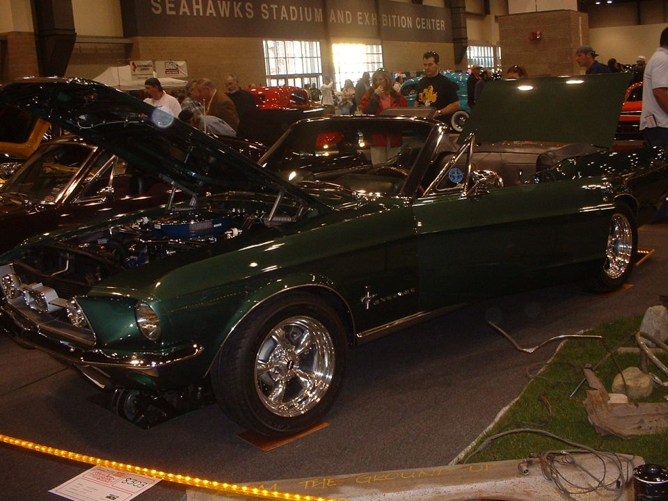Dark green classic Ford Mustang fastback with chrome wheels on display at an indoor car show