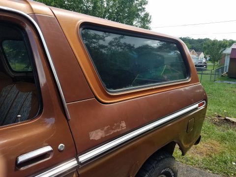 1979 Ford Bronco - Rear quarter panel of a brown Ford Bronco, showing side window and chrome trim.