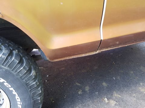 1979 Ford Bronco - Close-up of a brown 1978 Ford Bronco's side panel, showing rust and a large off-road tire.