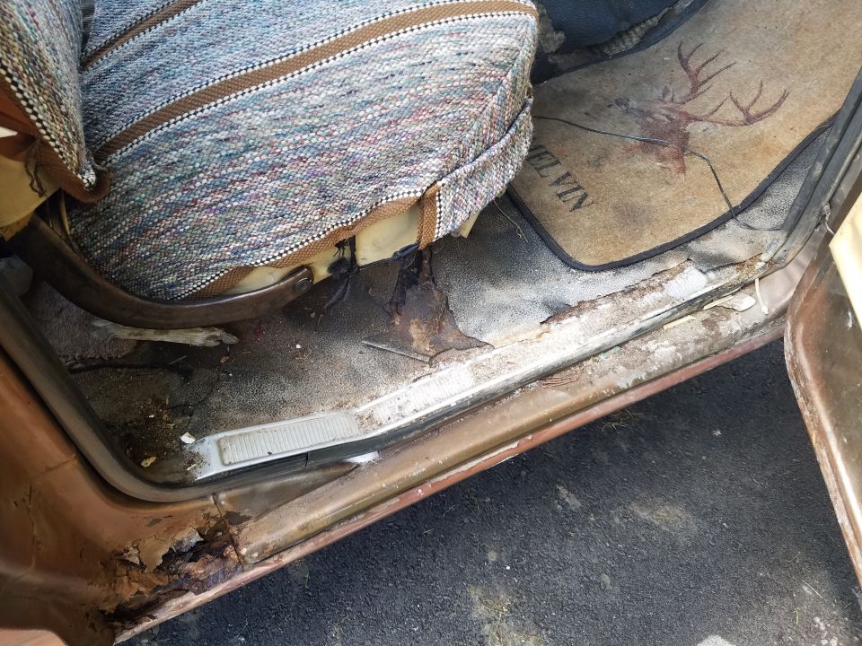 Interior door sill and floor mat of an old vehicle. Mat has a deer graphic and the name MELVIN