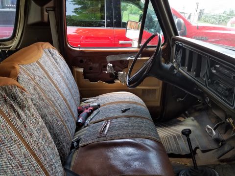1979 Ford Bronco - The interior of a vintage truck shows signs of wear and tear, with a red truck visible through the window.
