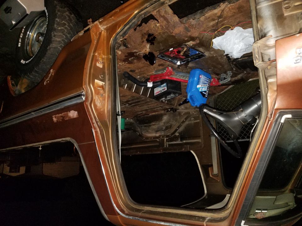 Interior of a rusty vehicle with tools and fluids on the floor. Steering wheel visible