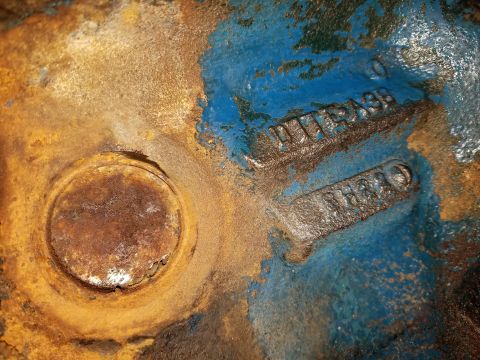1979 Ford Bronco - Close-up of a cast iron part with chipped blue and rust paint, revealing stamped numbers D1TA36 and 8H20.