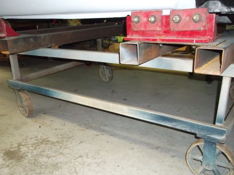 1967 Ford Mustang - A car body is seen resting on a metal dolly with red support brackets, indicating it is likely undergoing maintenance or restoration.