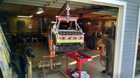 1985 Jeep CJ7 - A red Jeep-style vehicle is in a garage, with its engine being removed by an engine hoist.
