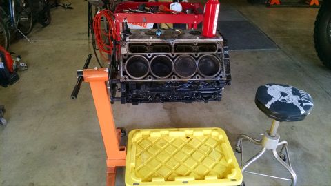 1985 Jeep CJ7 - Engine block on a stand in a garage, with a yellow drain pan and a stool nearby.