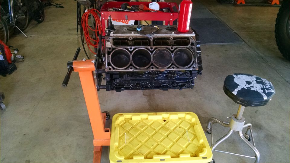 Engine block on an orange stand, with a yellow drain pan below