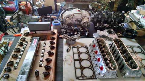 1985 Jeep CJ7 - Engine parts including cylinder heads and gaskets are organized on a workbench for assembly or repair.