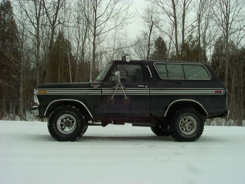 1978 Ford Bronco - A black 1978 Ford Bronco sits in a snowy landscape, its side profile clearly visible with distinctive chrome accents.