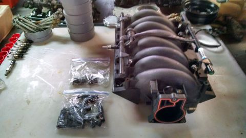 1985 Jeep CJ7 - A collection of engine parts, including an intake manifold and several fuel injectors, are organized on a table.