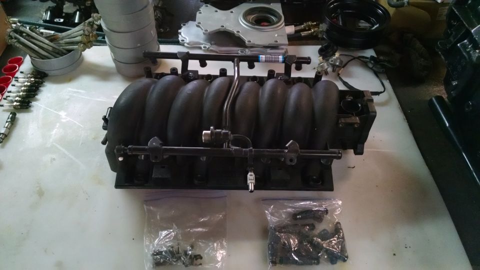 Black engine intake manifold with fuel injectors and hardware on a white surface