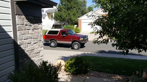 1996 Ford Bronco - Red 1996 Ford Bronco parked on a residential street with houses in the background.