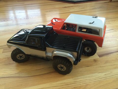 1989 Ford Bronco - Two remote control trucks are parked side-by-side on a wood floor.