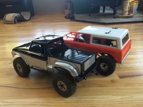 1989 Ford Bronco - Two remote-controlled toy trucks are parked side-by-side on a wooden floor.