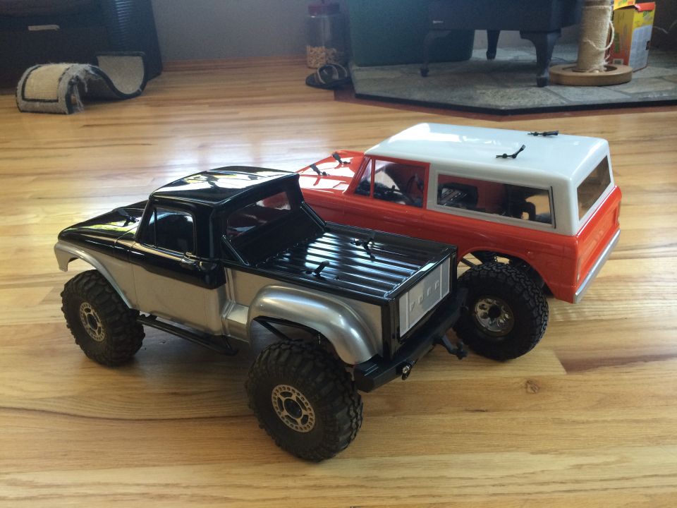 Two toy trucks, one black and silver pickup, one orange and white SUV, on a wooden floor