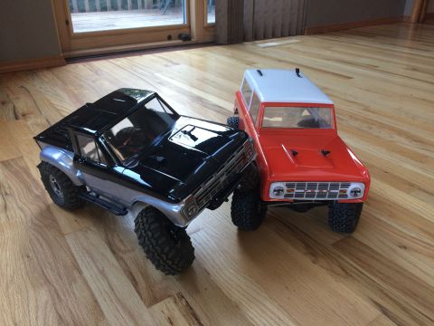1989 Ford Bronco - Two remote-controlled trucks, one black and silver and the other red and white, are positioned on a polished wooden floor.