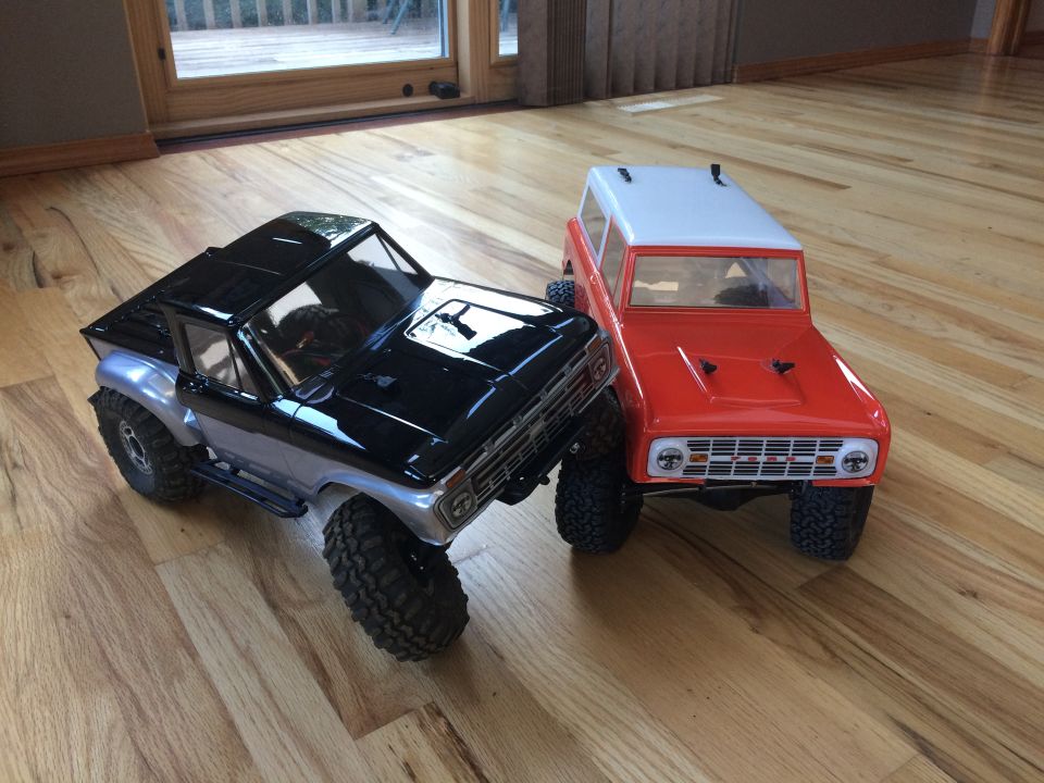 Black and silver RC truck next to red and white RC truck on wooden floor