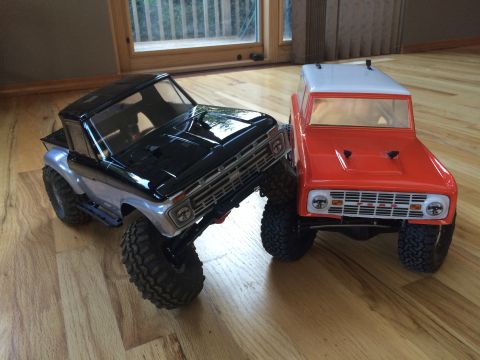 1989 Ford Bronco - Two remote control trucks are parked on a wooden floor, with one in front of the other.