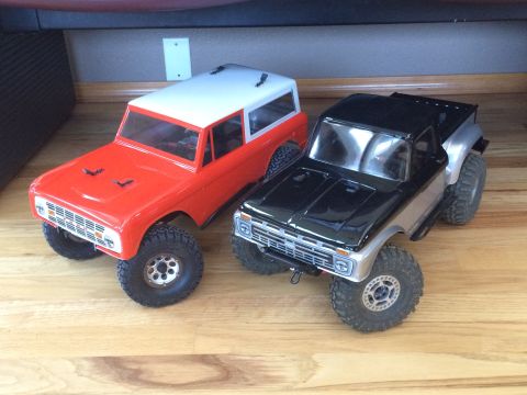 1989 Ford Bronco - Two RC toy trucks, a red Bronco-style SUV and a black pickup, are displayed on a wooden surface.