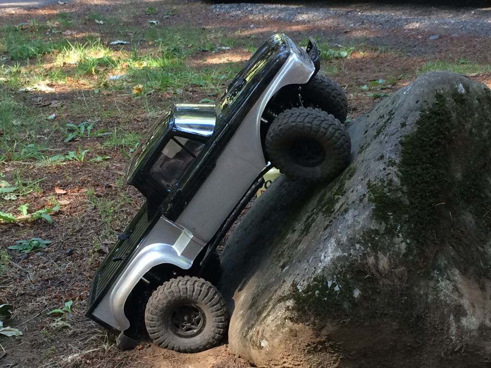 Black and silver RC crawler truck climbing a mossy rock in the woods