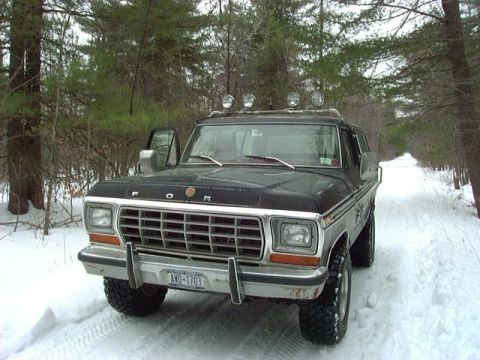 1978 Ford Bronco - A black 1978 Ford Bronco with roof-mounted lights sits on a snow-covered path in a wooded area.