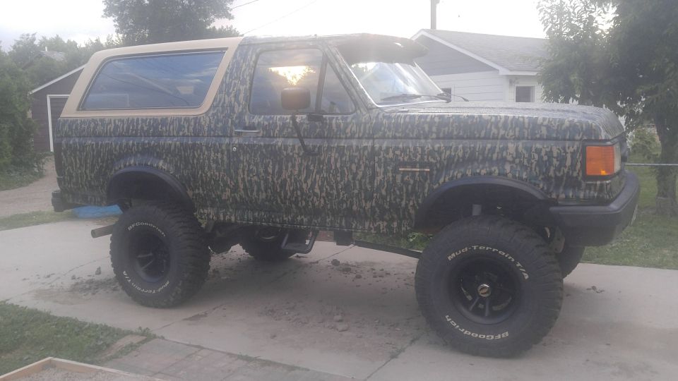 1991 Ford Bronco with camouflage wrap and lifted suspension, parked on a driveway
