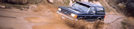 1991 Ford Bronco - A Ford Bronco navigates a challenging off-road course, kicking up mud and water.