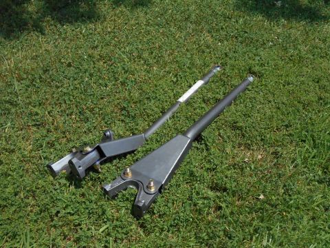 1972 Ford Bronco - Two dark gray metal linkage arms with bolts and brackets are lying on a grassy lawn. One arm has a white label near the top.