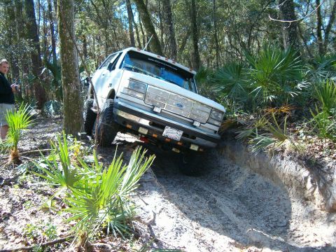 1991 Ford Bronco - A white 1991 Ford Bronco tackles a challenging off-road trail, demonstrating its capabilities.