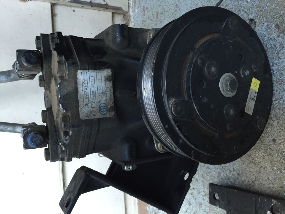 AC compressor with pulley clutch and a small ID label, photographed on the ground