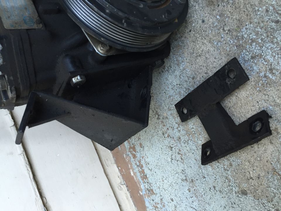 AC compressor mounting bracket and a black H-shaped metal plate on concrete