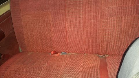 1988 Ford Bronco - The interior of a vehicle shows a red fabric rear seat with visible seatbelts and a watermark.