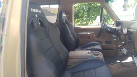 1991 Ford Bronco - Two black Corbeau bucket racing seats installed in a truck cab with tan interior and steering wheel.