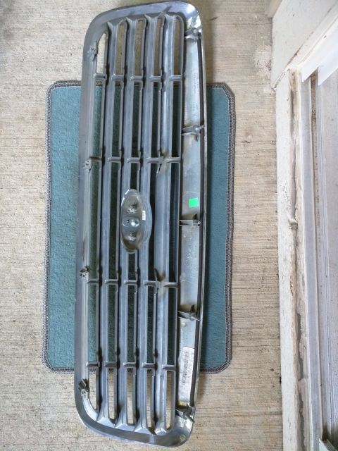 2007 Ford Crown Victoria - A chrome and black front grille is shown lying flat on a textured mat. The grille has vertical bars with a central emblem.