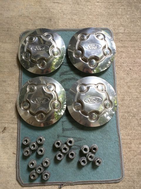 2007 Ford Crown Victoria - Four chrome Ford hubcaps with the Ford logo are laid out on a teal mat next to a collection of lug nuts.