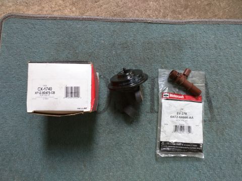 2007 Ford Crown Victoria - Two automotive parts, an EGR valve in its original box and a Motorcraft PCV valve in its packaging, are laid out on a blue-green textured m…