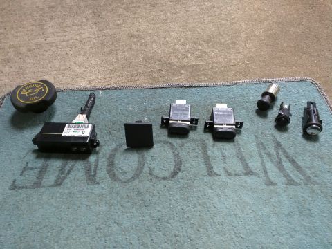 2007 Ford Crown Victoria - Several automotive parts are laid out on a teal welcome mat. Visible items include an engine oil cap, a black electronic module, a square b…